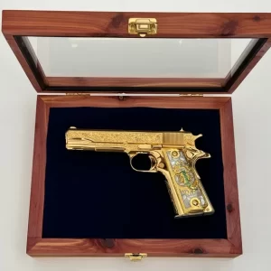 Luxury gold-finished engraved pistol resting in navy velvet inside a glass-top wooden case.