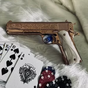 Gold custom Colt firearm with pearl grips displayed alongside playing cards and poker chips.