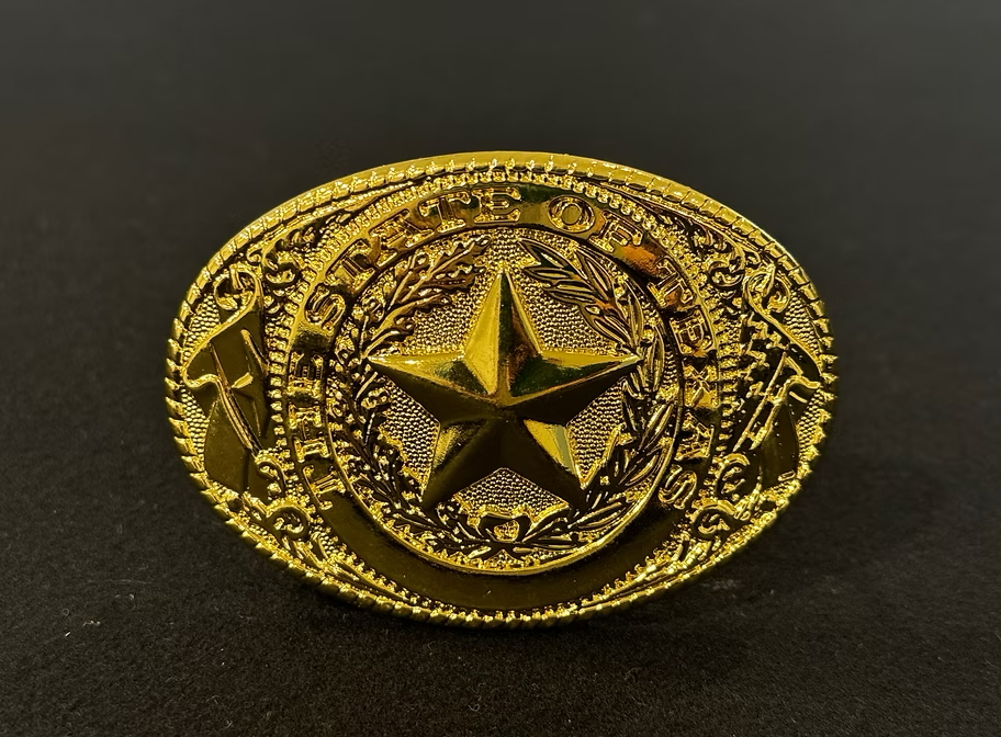 A polished cowboy belt buckle with a detailed design of the State of Texas.
