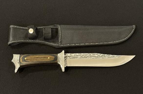 Bowie knife with dark wooden handle and patterned blade alongside black fabric sheath.