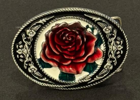 A cowgirl buckle engraved with silver and a rose with a deep red color.