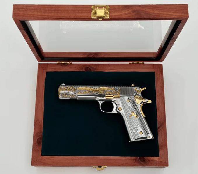 Custom electroplated 1911 with gold detailing showcased in a wooden display case